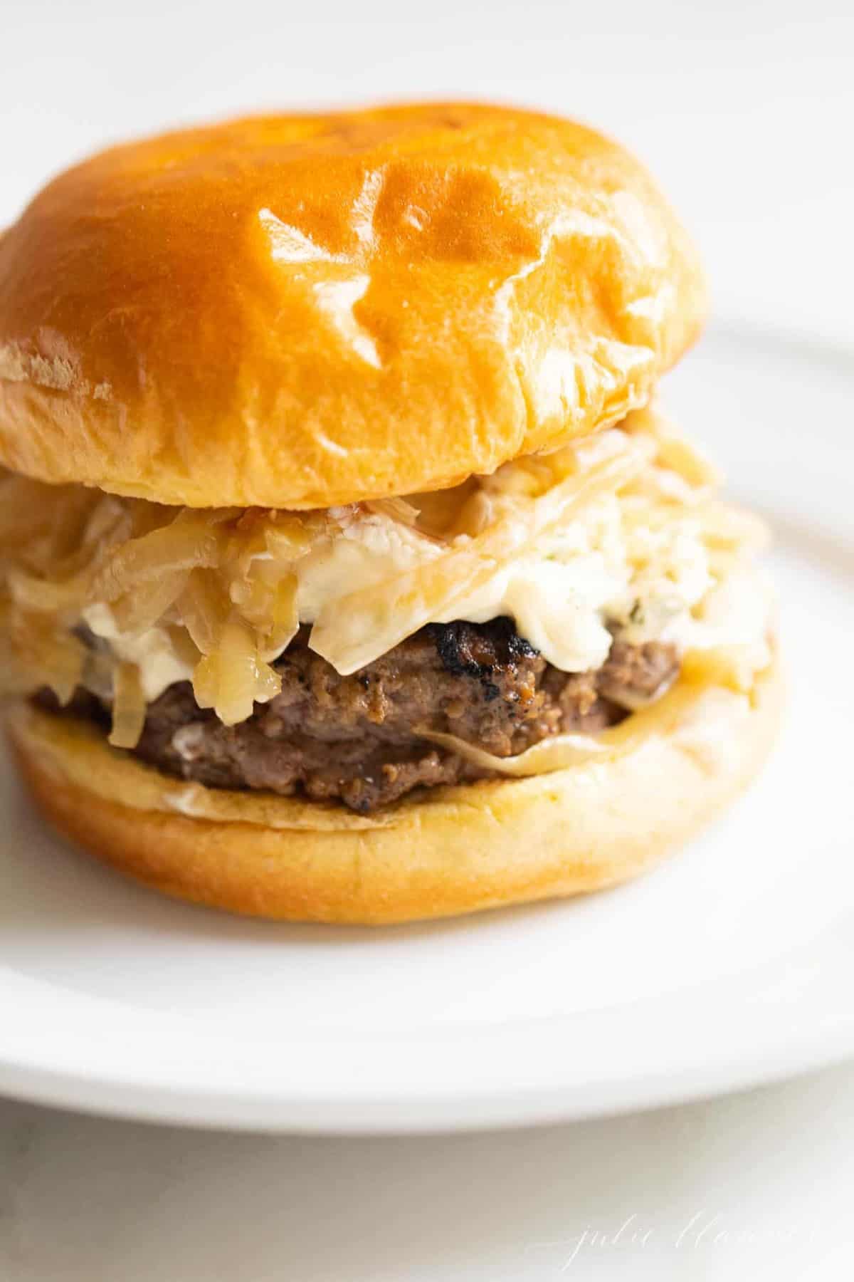 A gourmet burger on a white plate with a white background. 