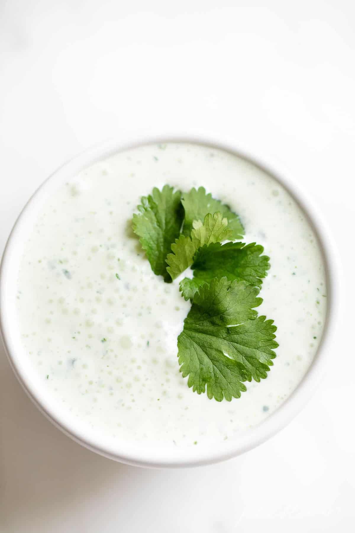 White surface with a bowl of cilantro crema with a few cilantro leaves on top.