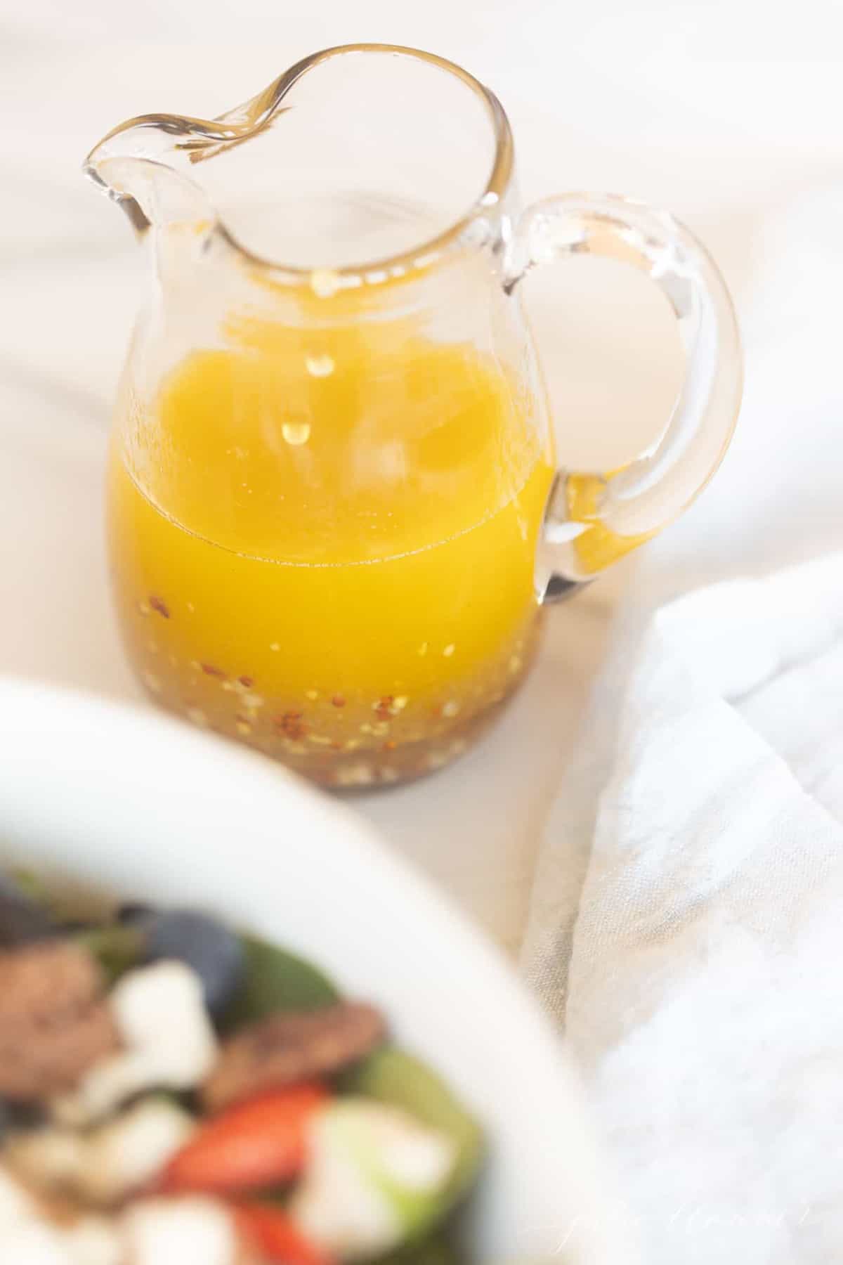 A white surface, clear pitcher full of homemade champagne vinaigrette