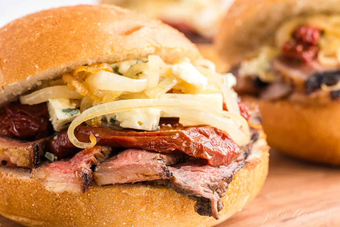 Close up of a steak sandwich on a bun, stacked with toppings.