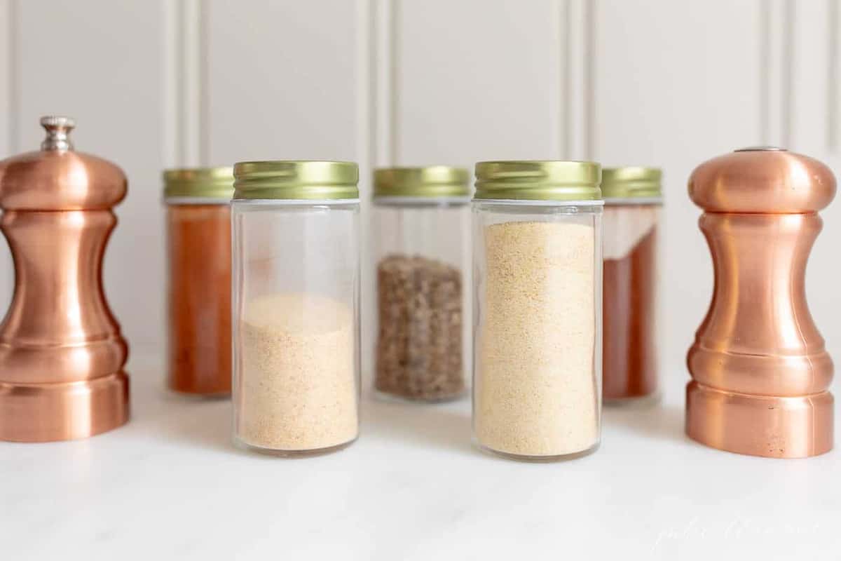 A white background with glass bottles of spices preparing to make blackened chicken seasoning.