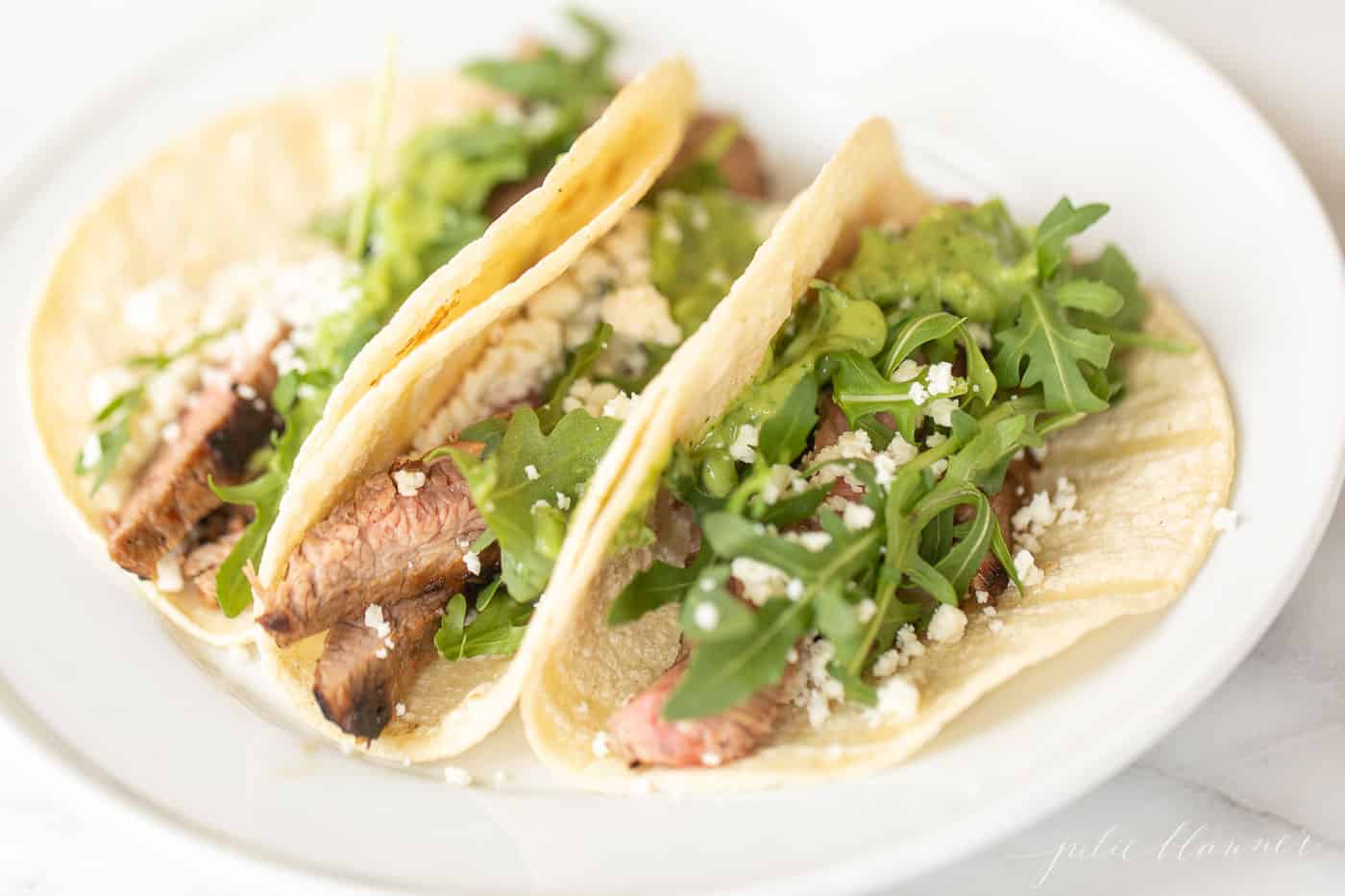 White plate with three small carne asada tacos.