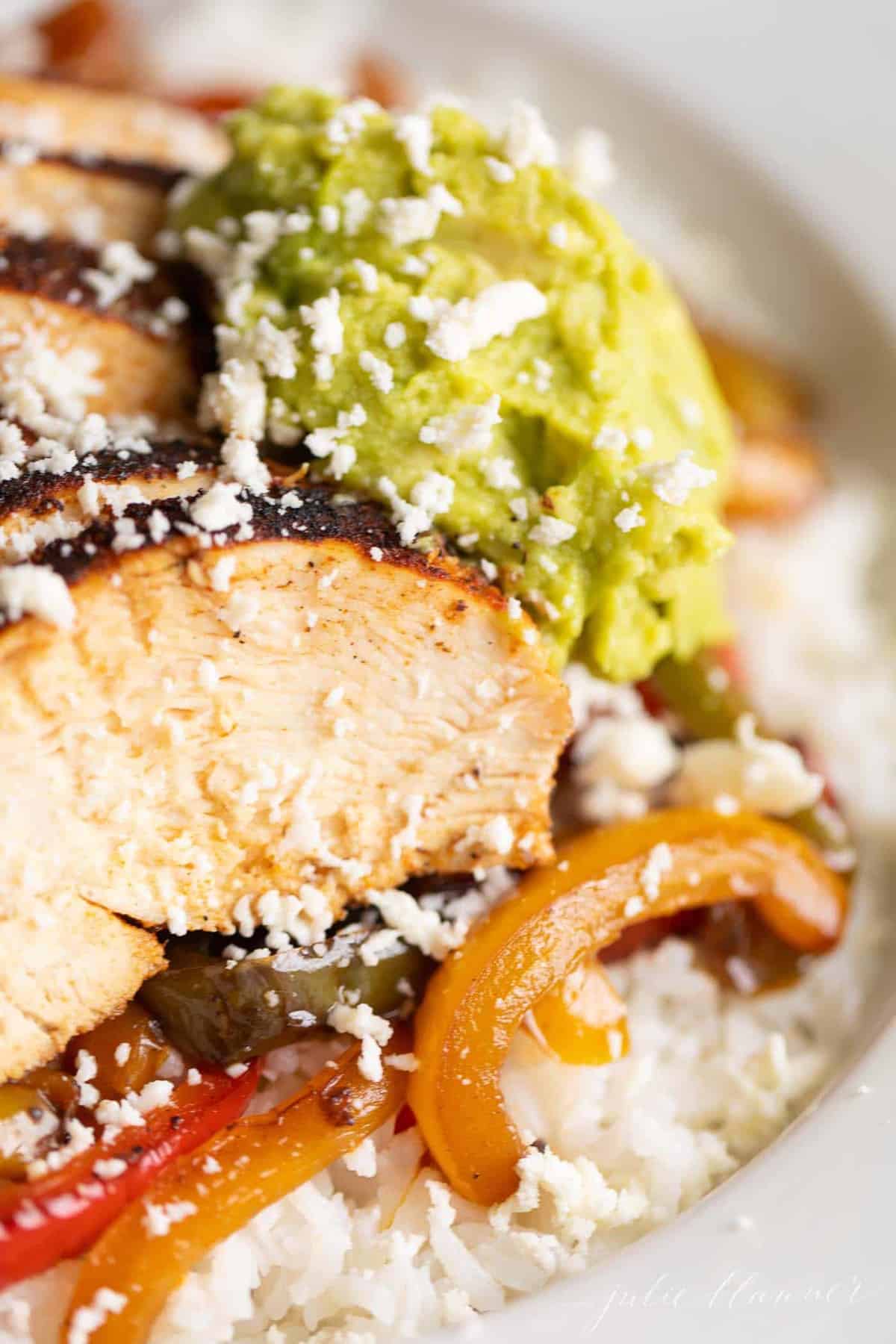 Close up of a chicken fajita bowl, crumbled cheese and guacamole on top.