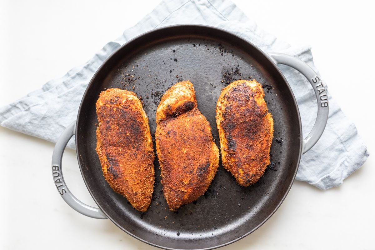 A cast iron pan with blackened chicken breasts.