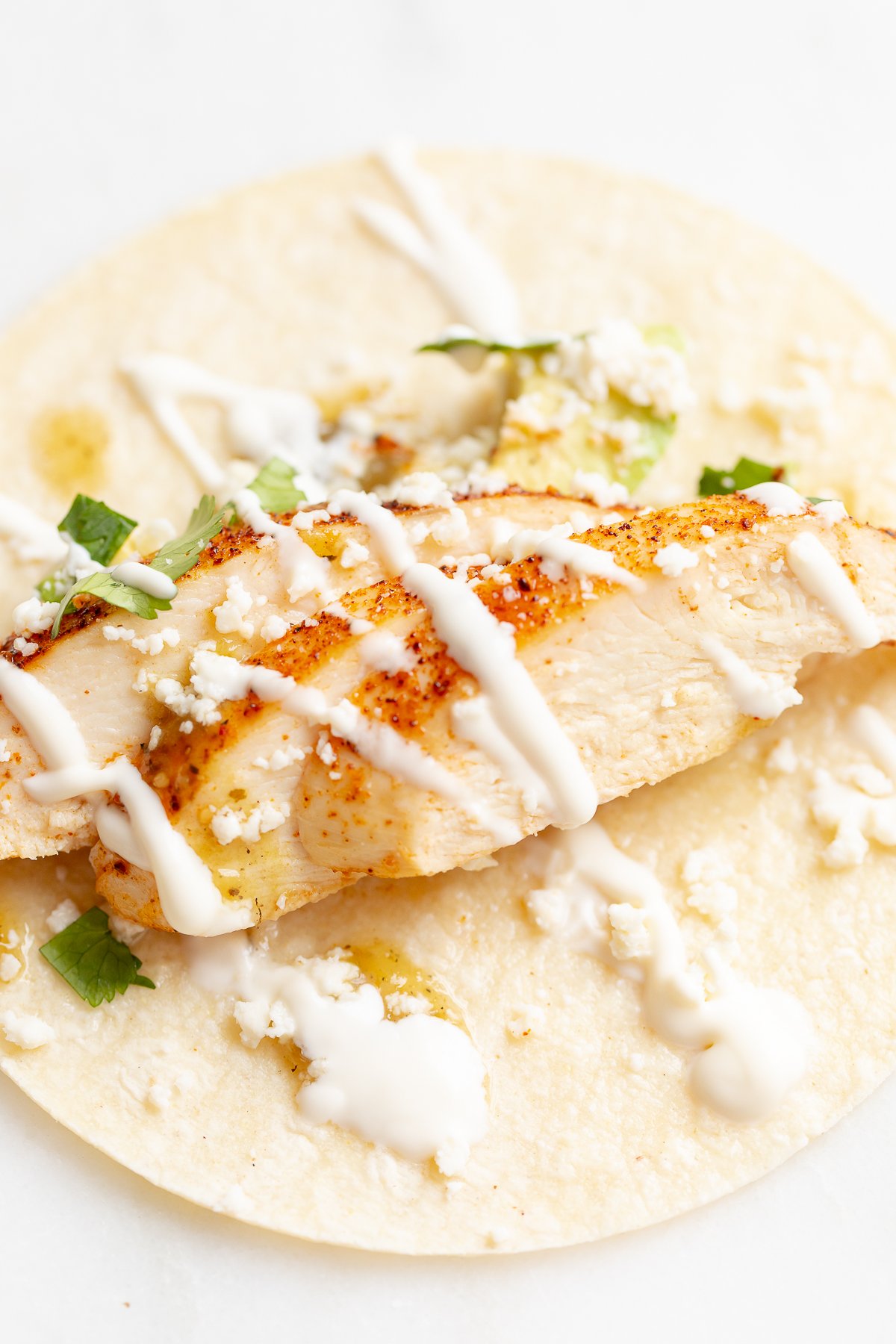 Chicken tacos in corn tortillas on a white surface.