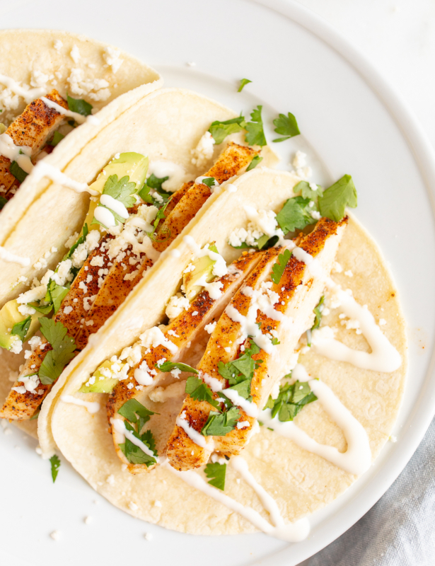 Chicken tacos in corn tortillas on a white surface.