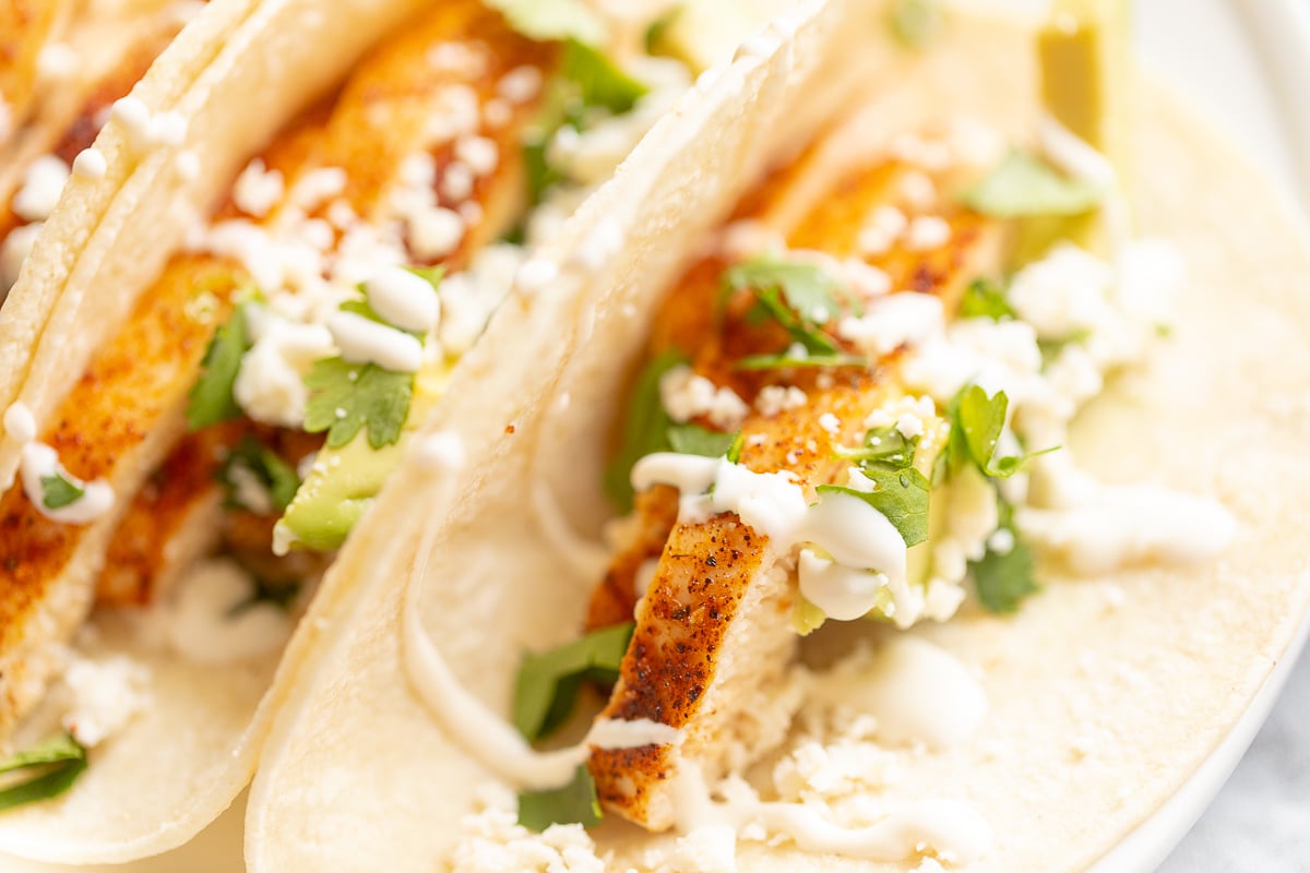 Chicken soft tacos in corn tortillas on a white surface.
