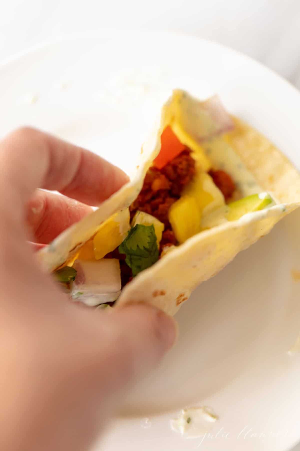 A single hand holding a single chorizo taco in a soft corn tortilla.