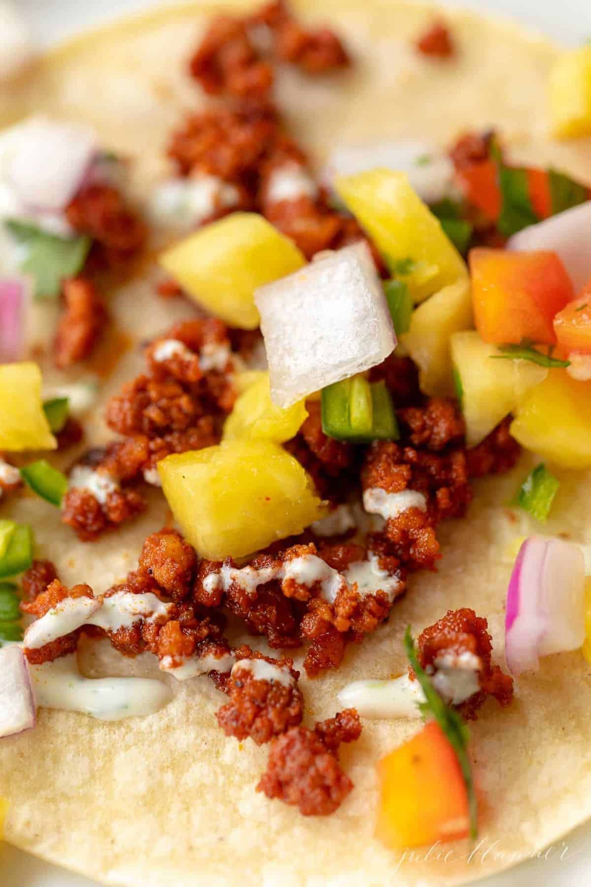 Close up of a chorizo taco topped with pineapple salsa and cilantro lime crema.