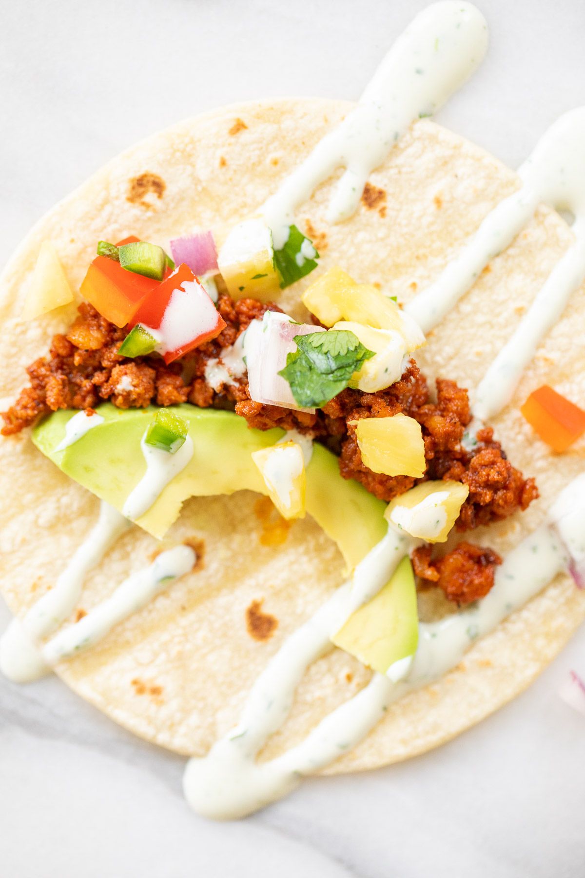 A chorizo taco topped with avocado, pineapple and lime crema.