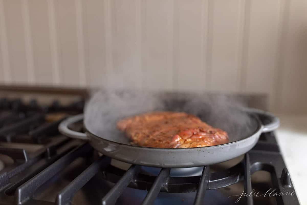 A cast iron pan on the stove, cooking flank steak.