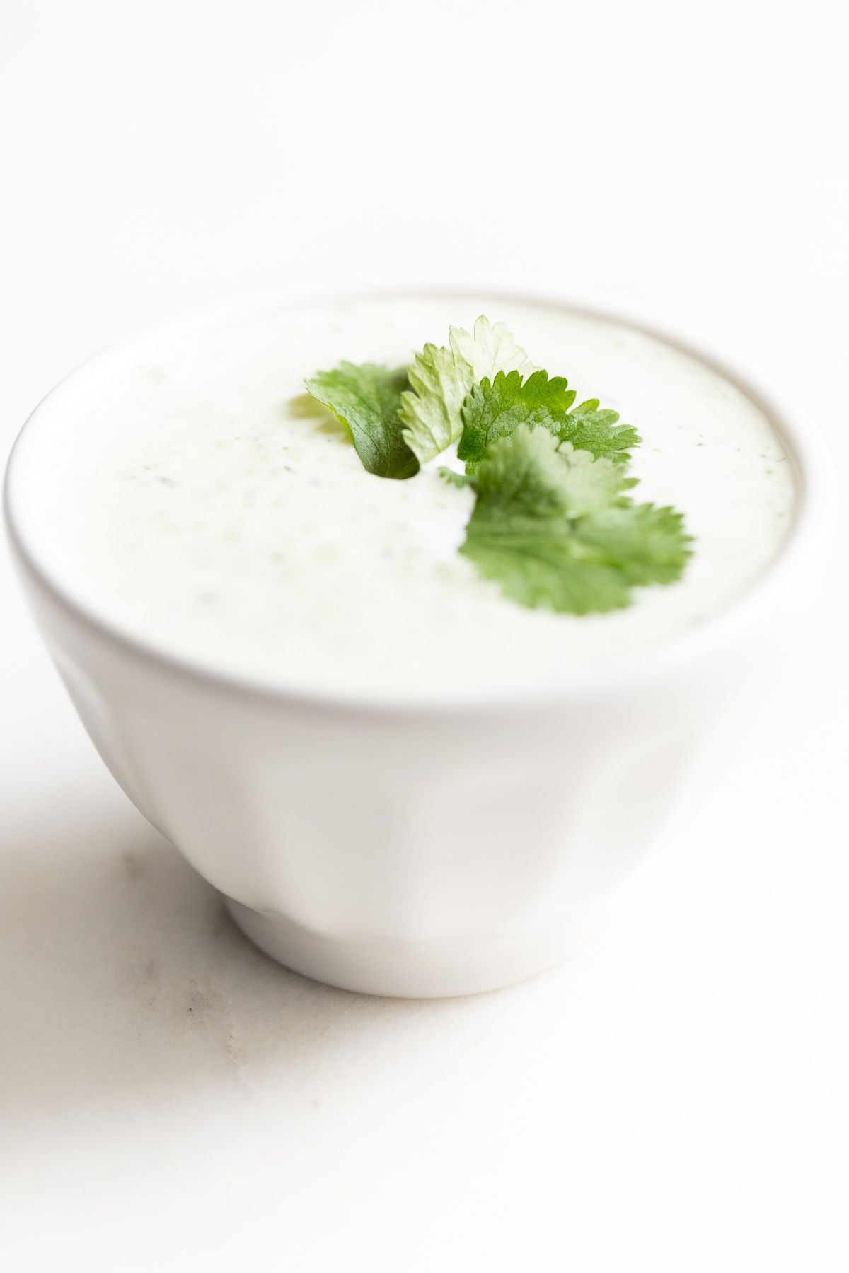 A white bowl of crema de cilantro on a white countertop, garnished with cilantro.
