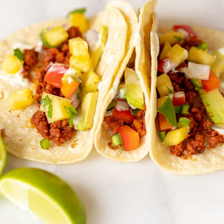 Three corn tortillas on a white surface, chorizo taco ingredients in each one.