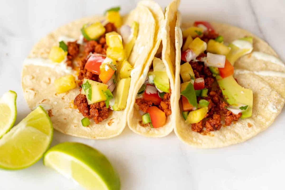 Three corn tortillas on a white surface, chorizo taco ingredients in each one.