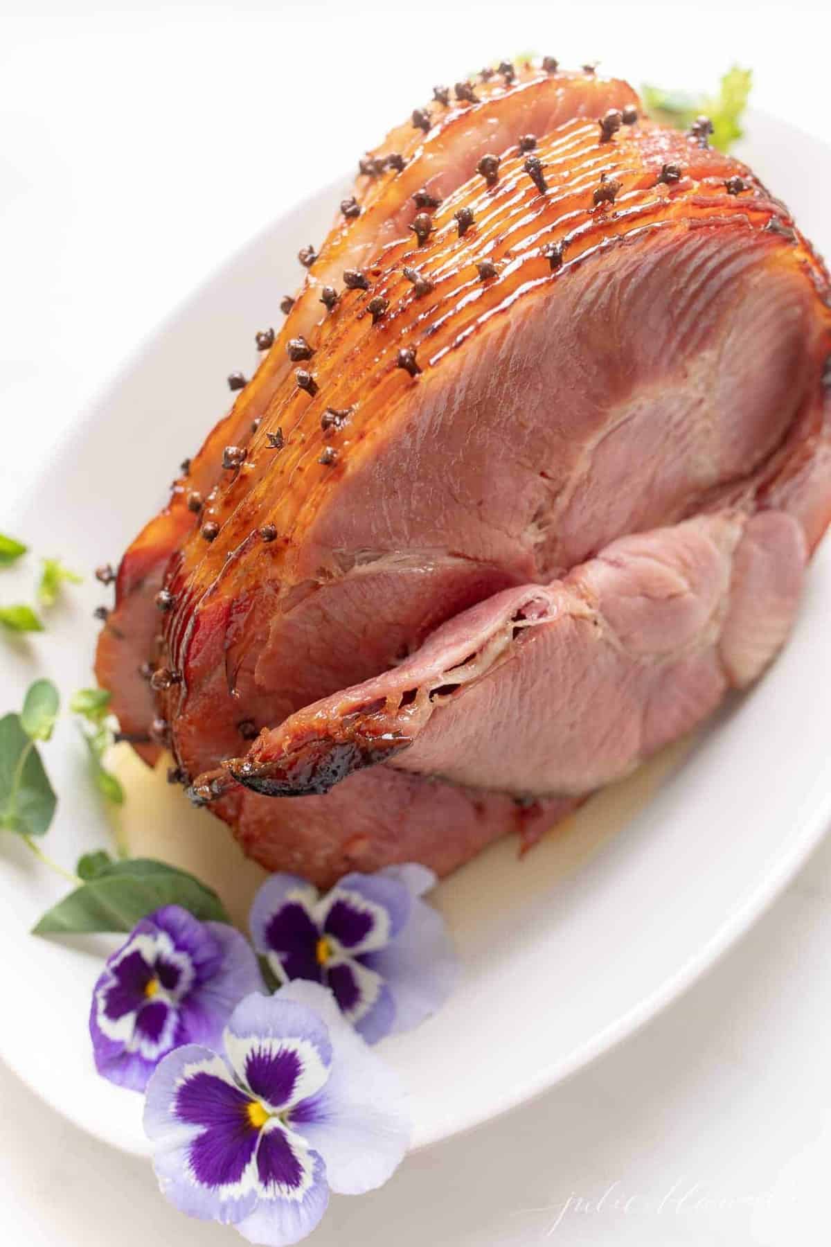 Sliced glazed ham, flowers to the side on a white platter.