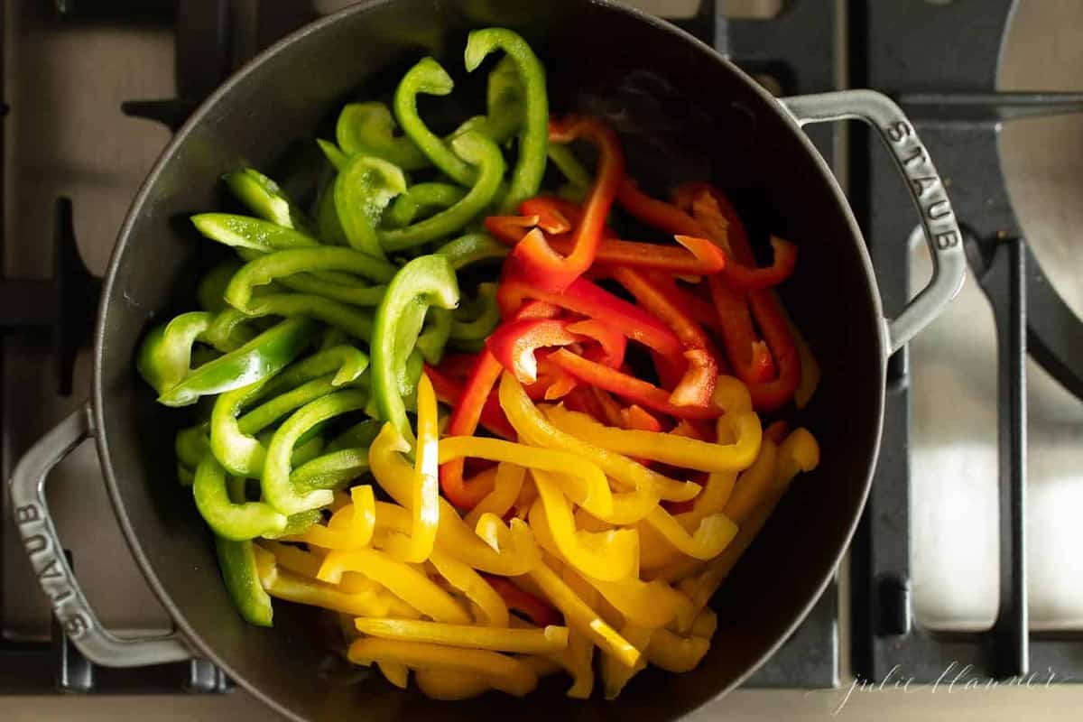 Red, green, and yellow bell peppers cut in a pan on the stovetop. 