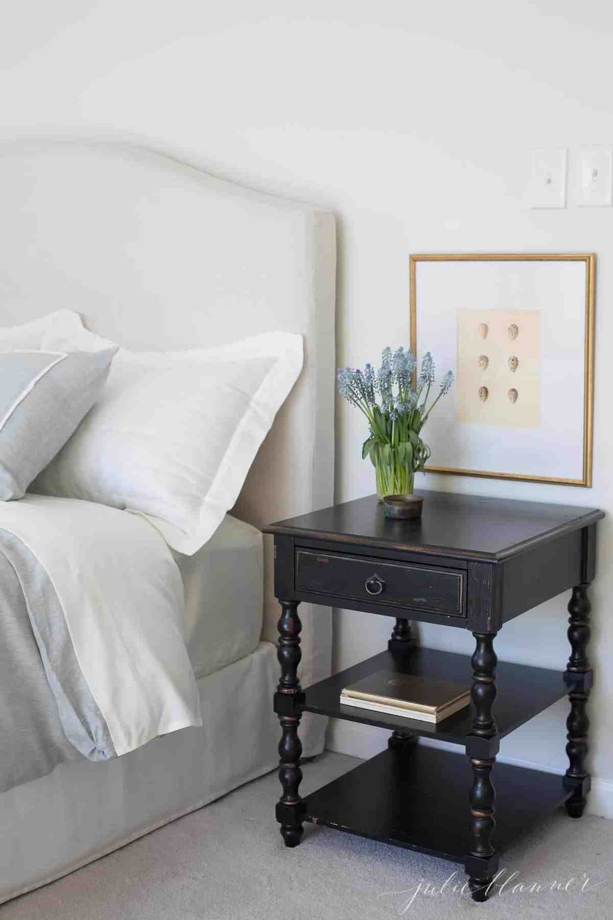 A white bedroom with spring decor like a vase of flowers and spring artwork on the wall. 