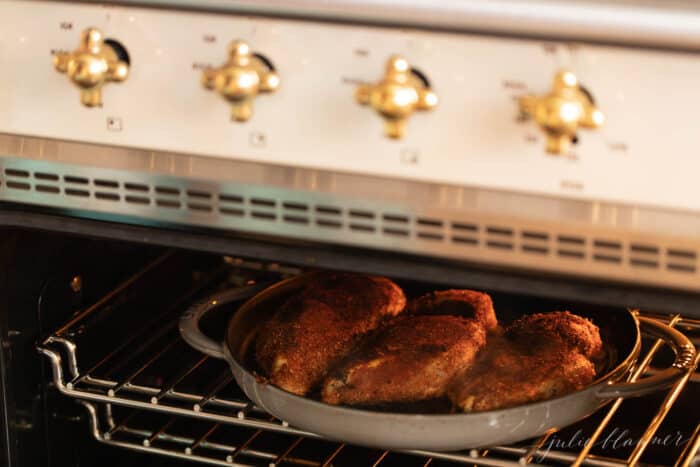 A cast iron pan with three blackened chicken breasts inside the oven.