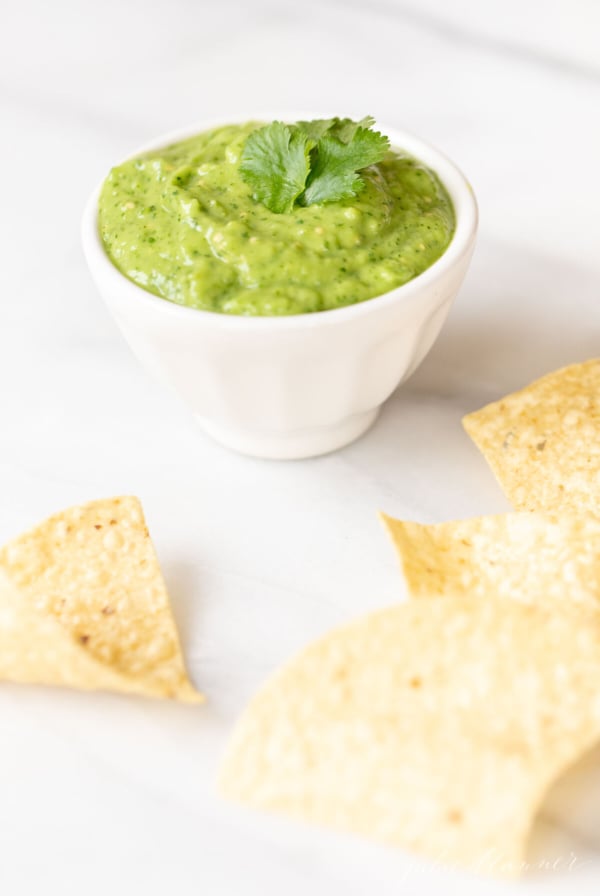 A white bowl of salsa guacamole surrounded by tortilla chips.