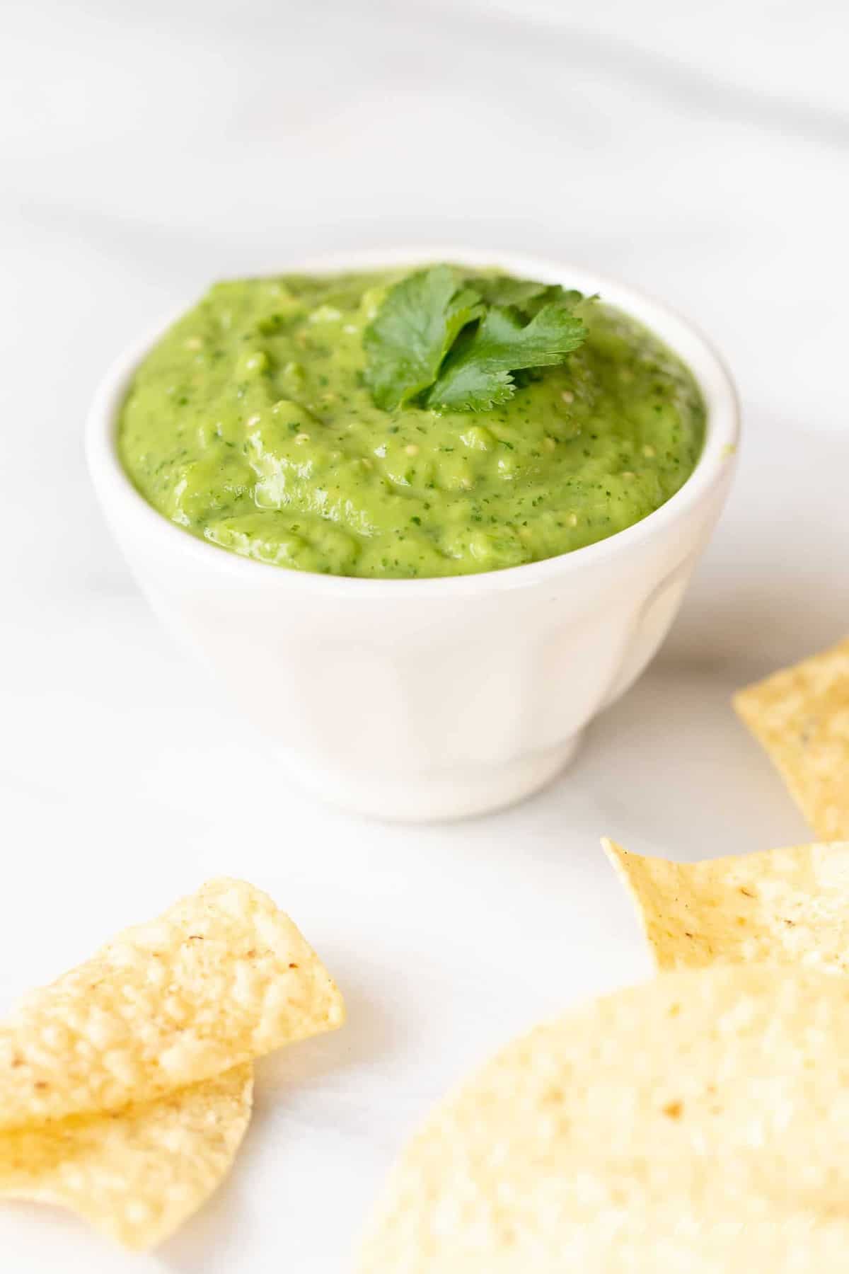 A white bowl of avocado sauce, tortilla chips scattered around.