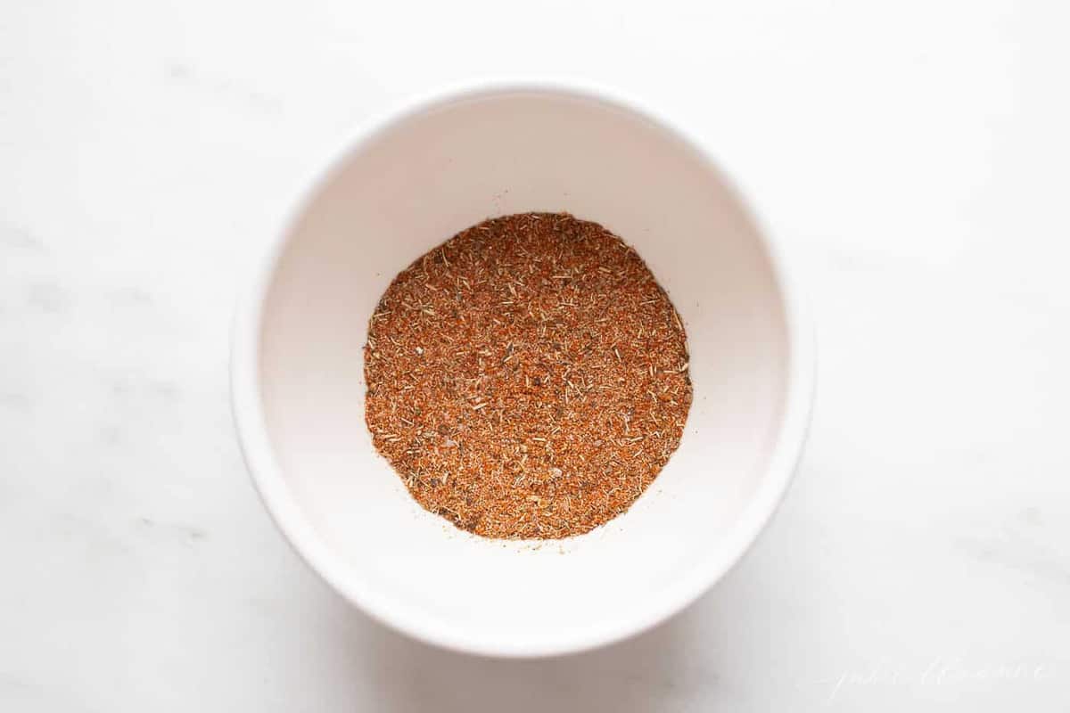 White surface with a small white bowl full of blackening spice blend.