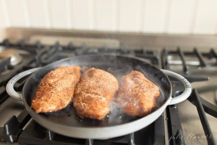 A cast iron pan with three blackened chicken breasts on the stove top.
