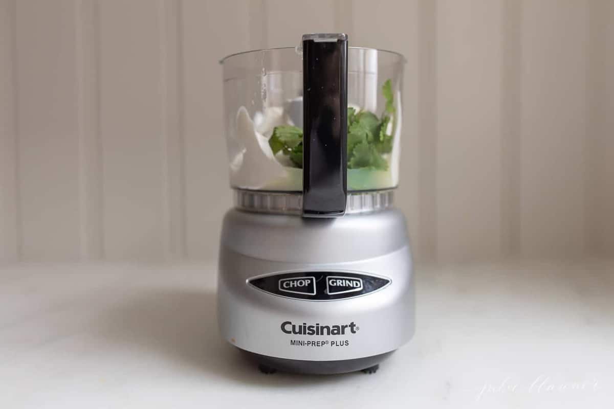 White kitchen with a food processor filled with lime cilantro crema mixture.