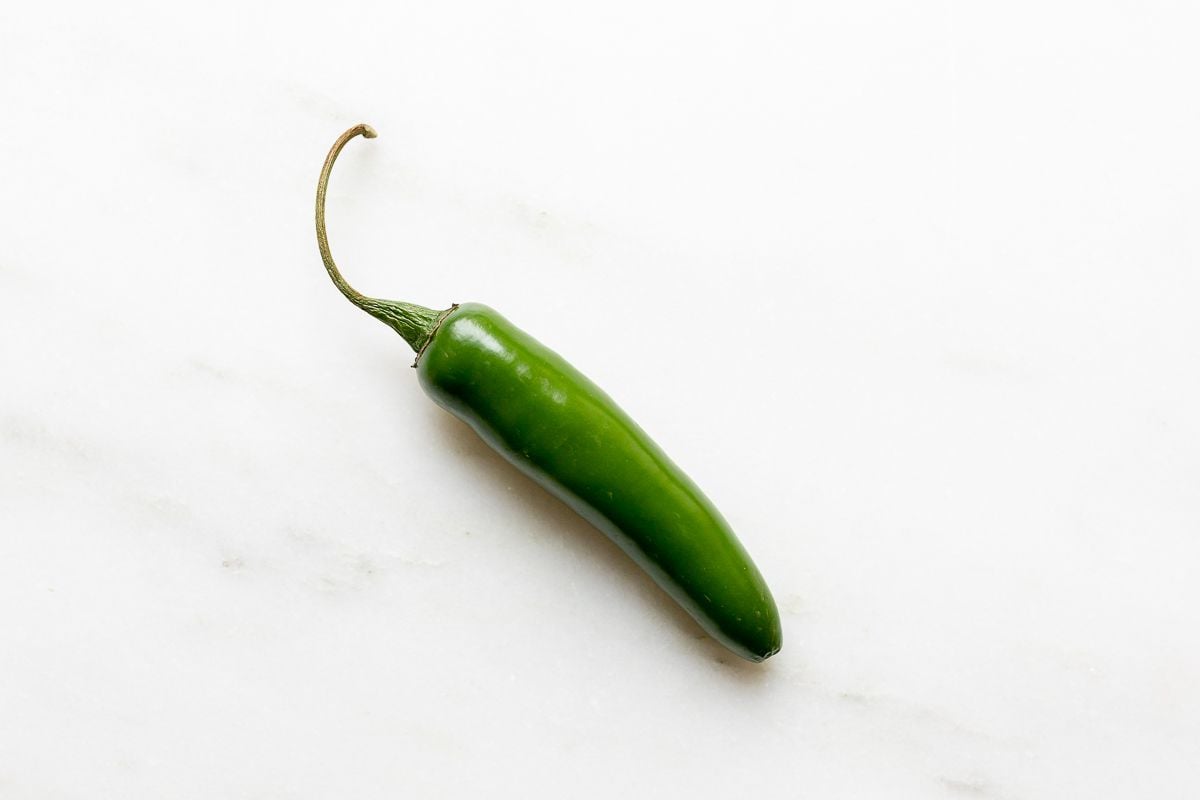 A single jalapeno on a white marble surface