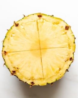 A pineapple, sliced in half and scored across the middle.