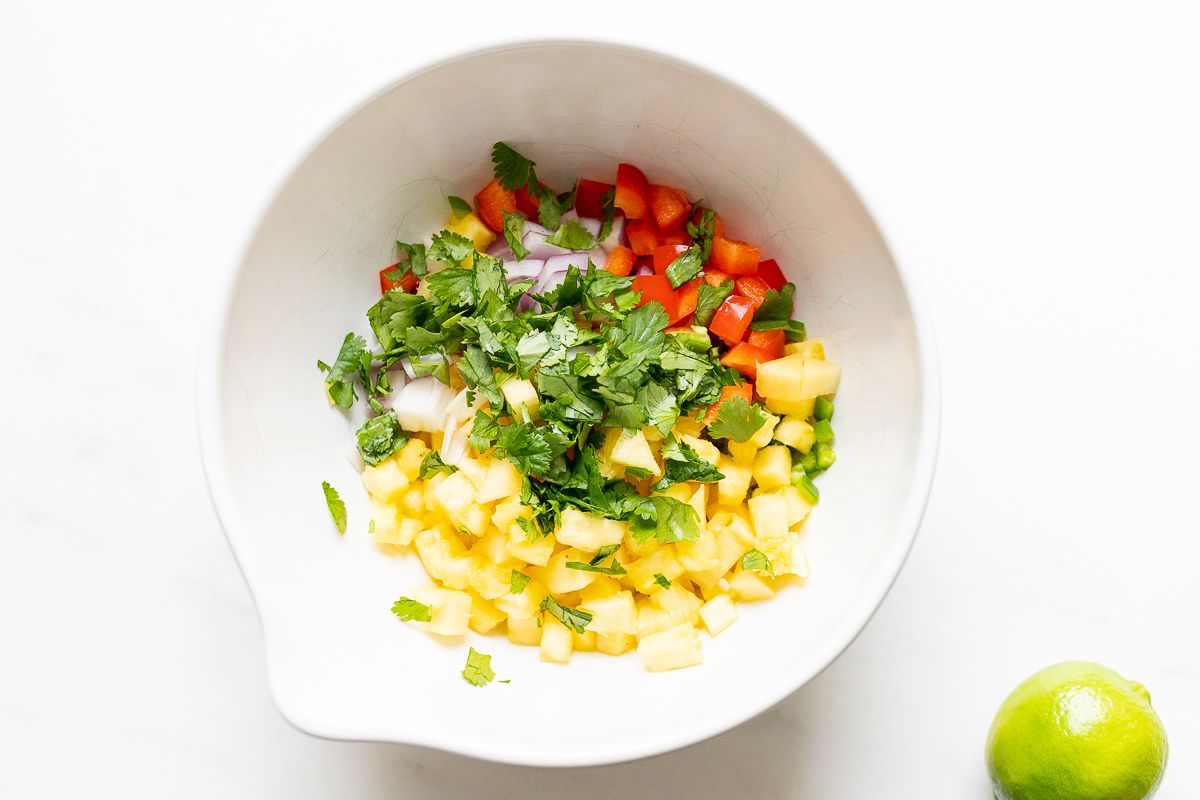 Ingredients for pineapple salsa, organized in a white bowl before mixing.
