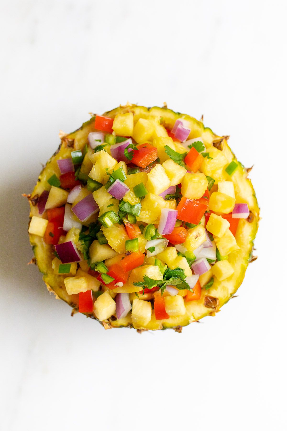 Pineapple salsa inside a pineapple bowl, on a white countertop.