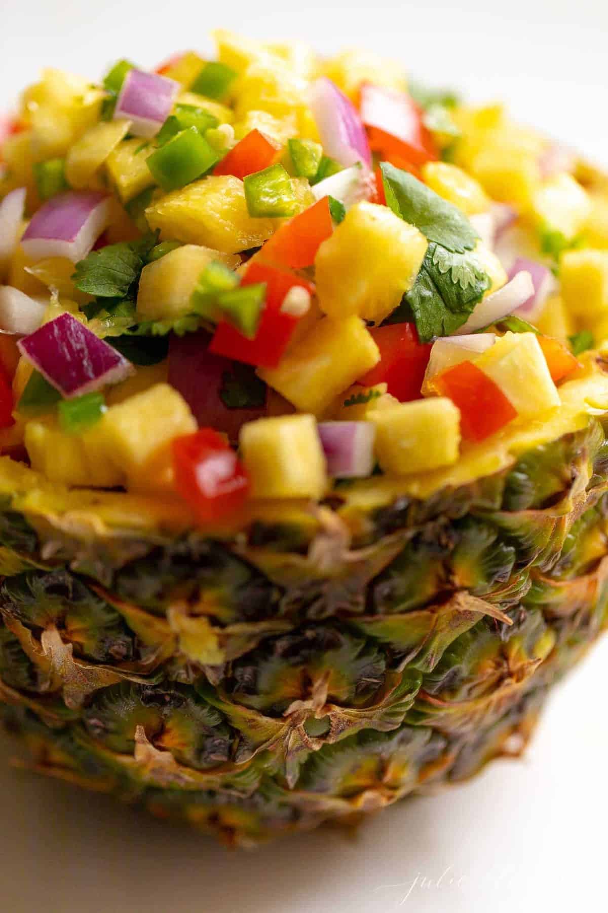 A fresh bowl made from a cut pineapple, filled with pineapple salsa.