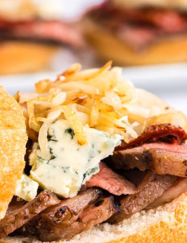A steak sandwich with onion straws and cheese on top, top bun balanced to the side.