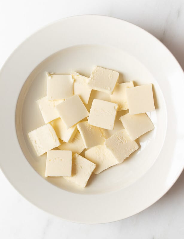 A white surface, with a white plate full of cuts of cold butter.