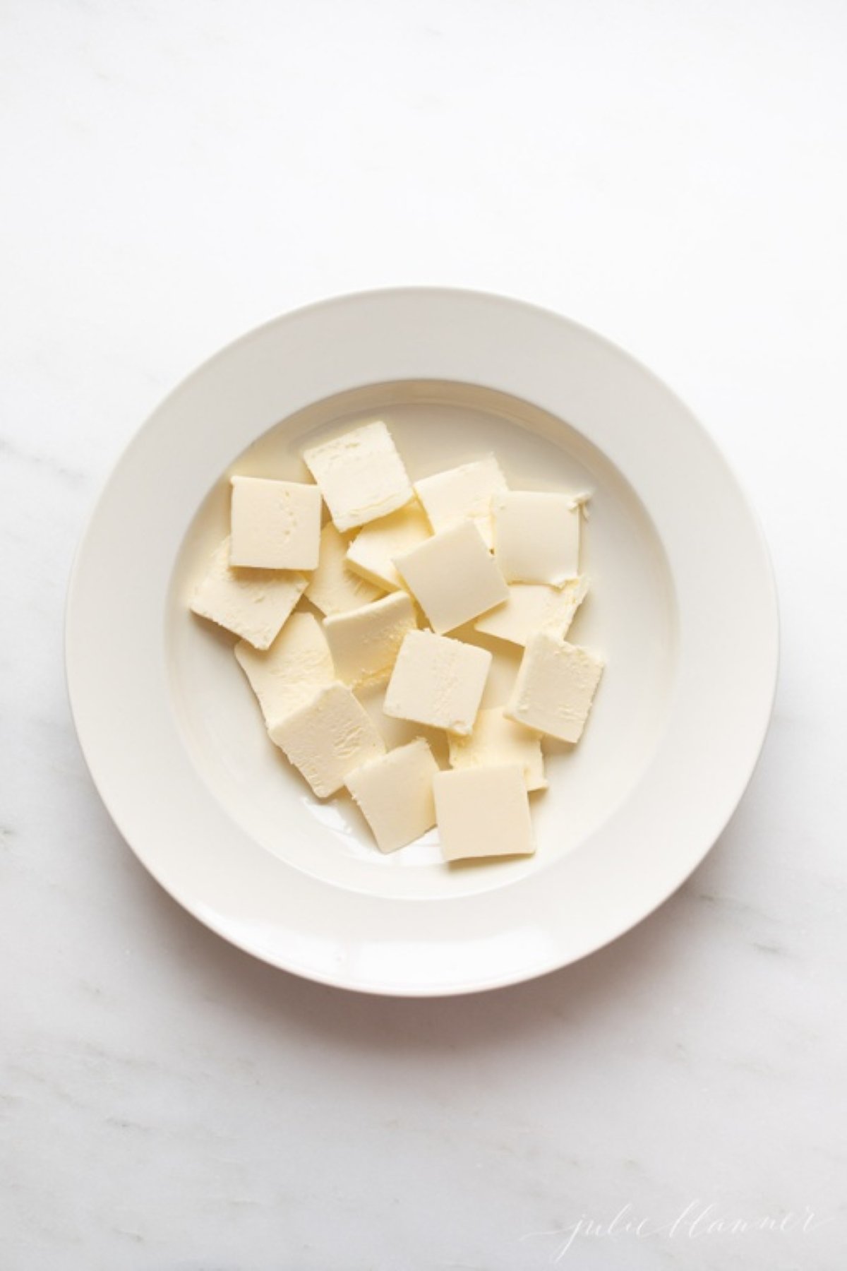 A white plate full of pats of butter in a tutorial for how to soften butter quickly.