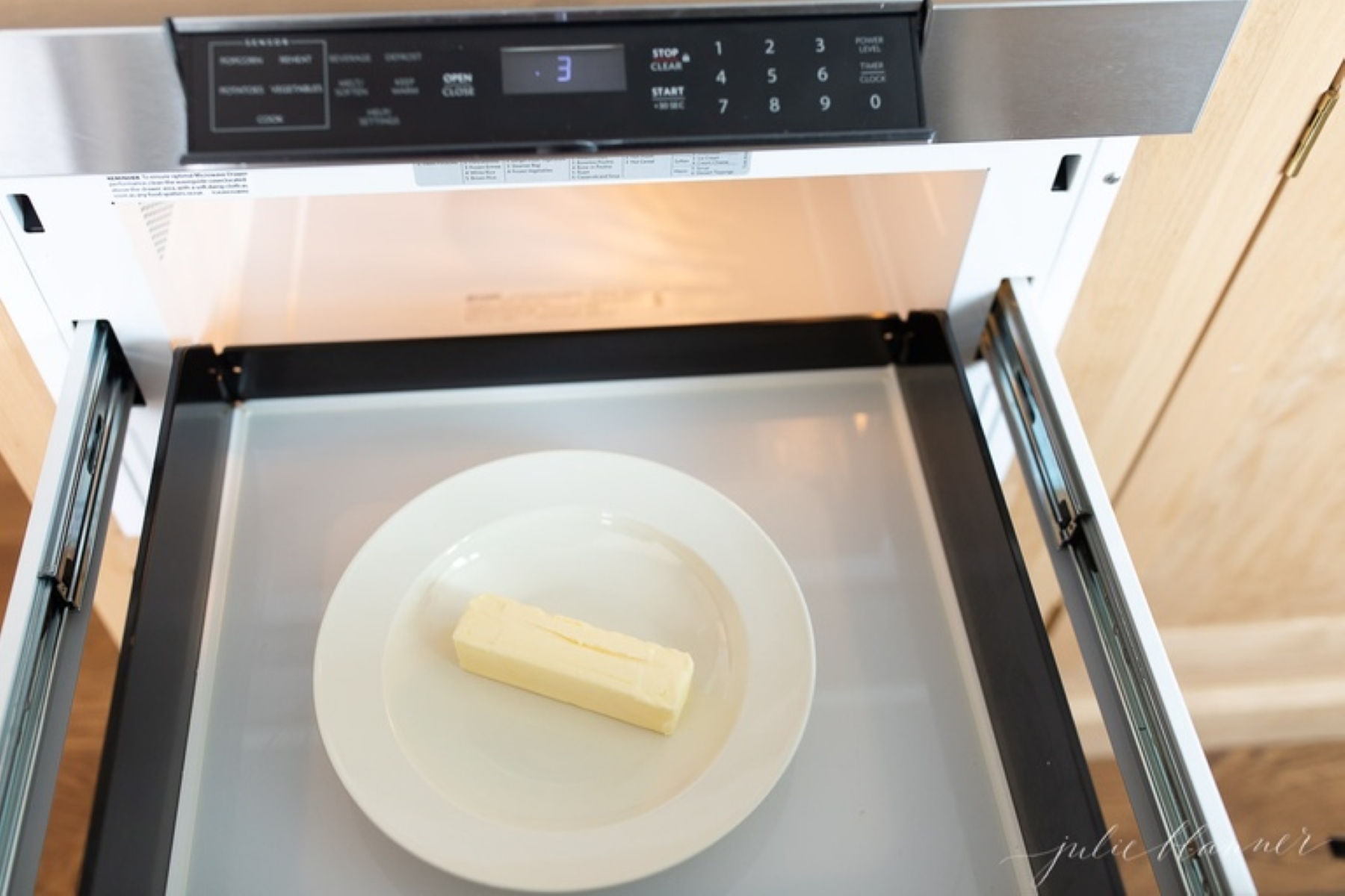 A single stick of butter on a white plate in a drawer microwave.
