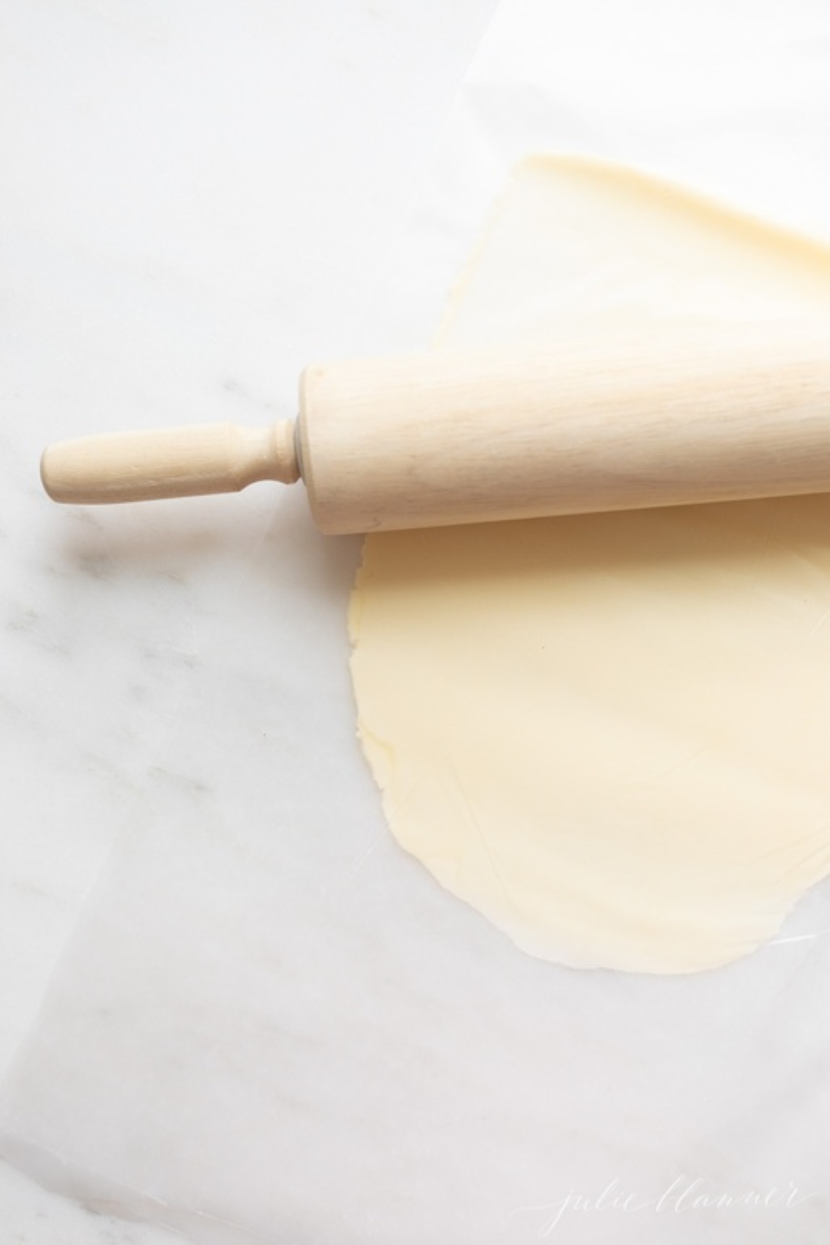 A wooden rolling pin next to a stick of butter that's flattened in between two sheets of waxed paper.