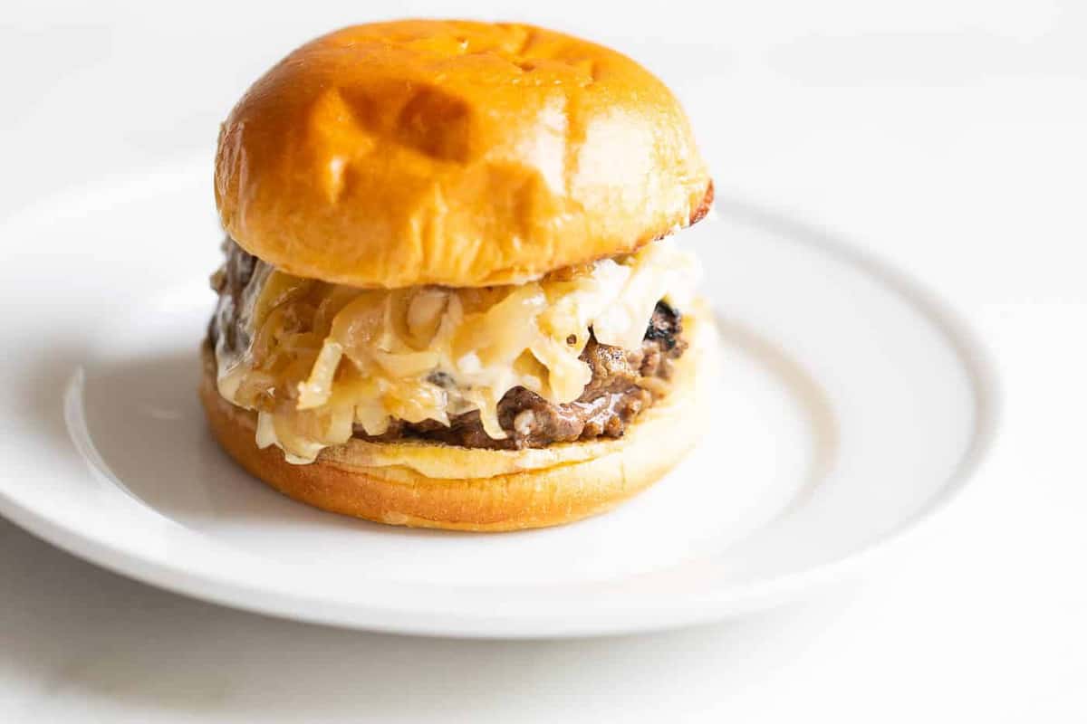 A gourmet burger on a white plate with a white background. 