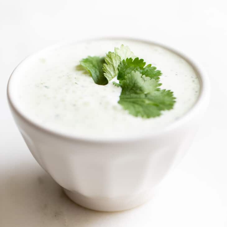 White surface with a bowl of crema de cilantro with a few cilantro leaves on top.
