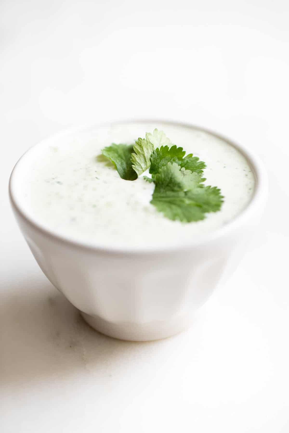 Crema de Cilantro Lime in a white bowl, garnished with cilantro, on a white surface. 