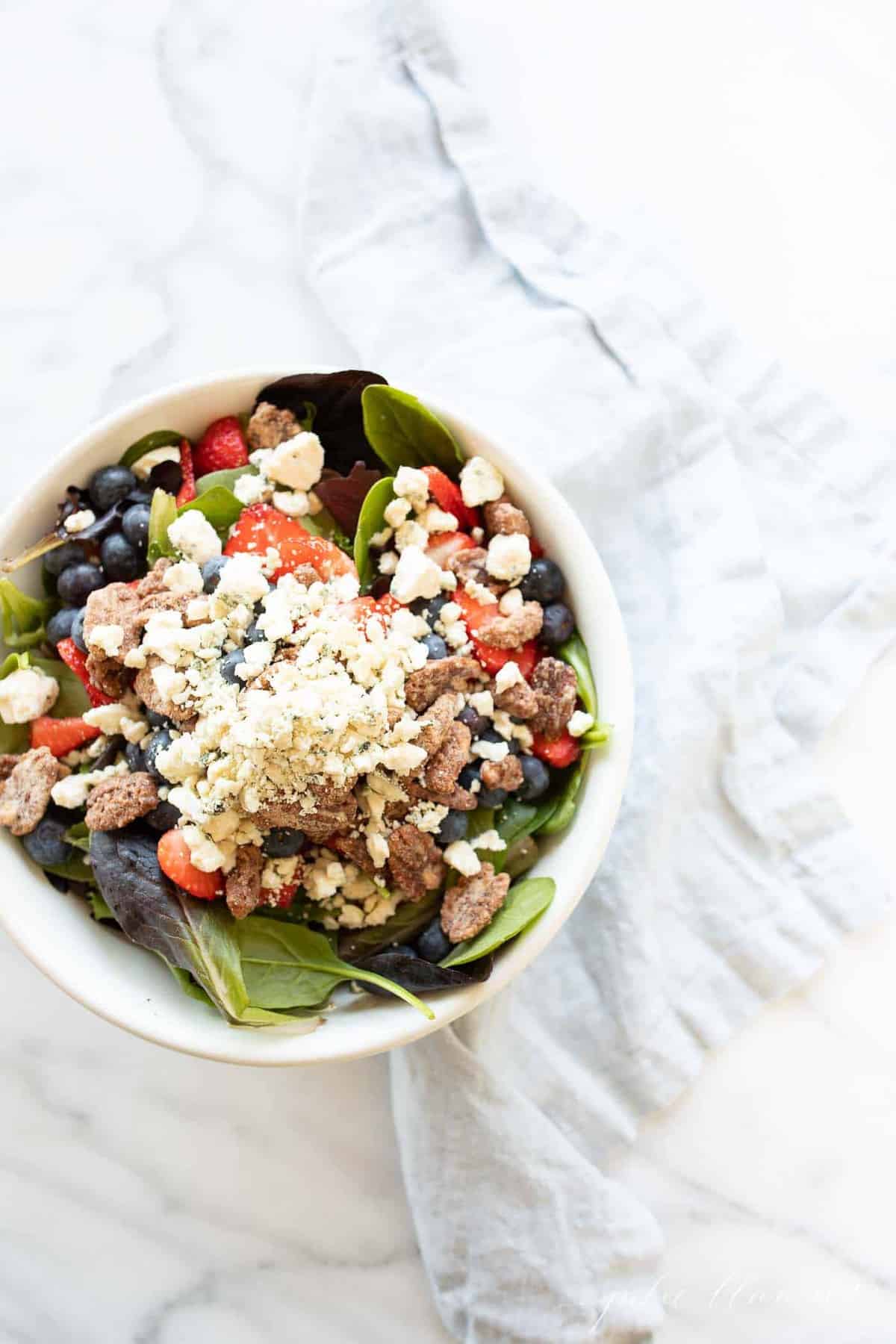 A white bowl full of a fresh spring mix with berries and nuts