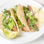 Carne asada tacos, topped with cilantro on a white plate.