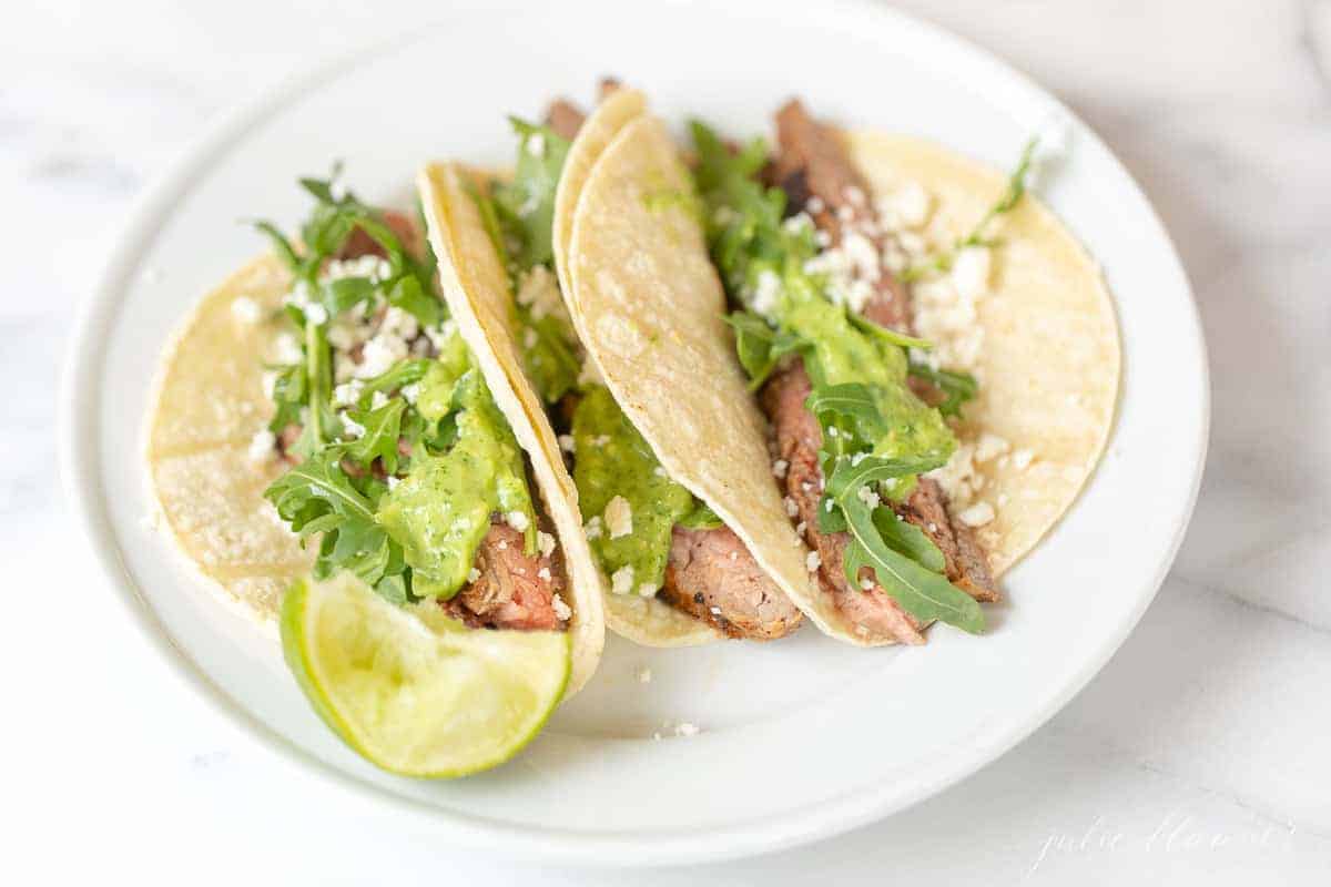Carne asada tacos, topped with cilantro on a white plate. 