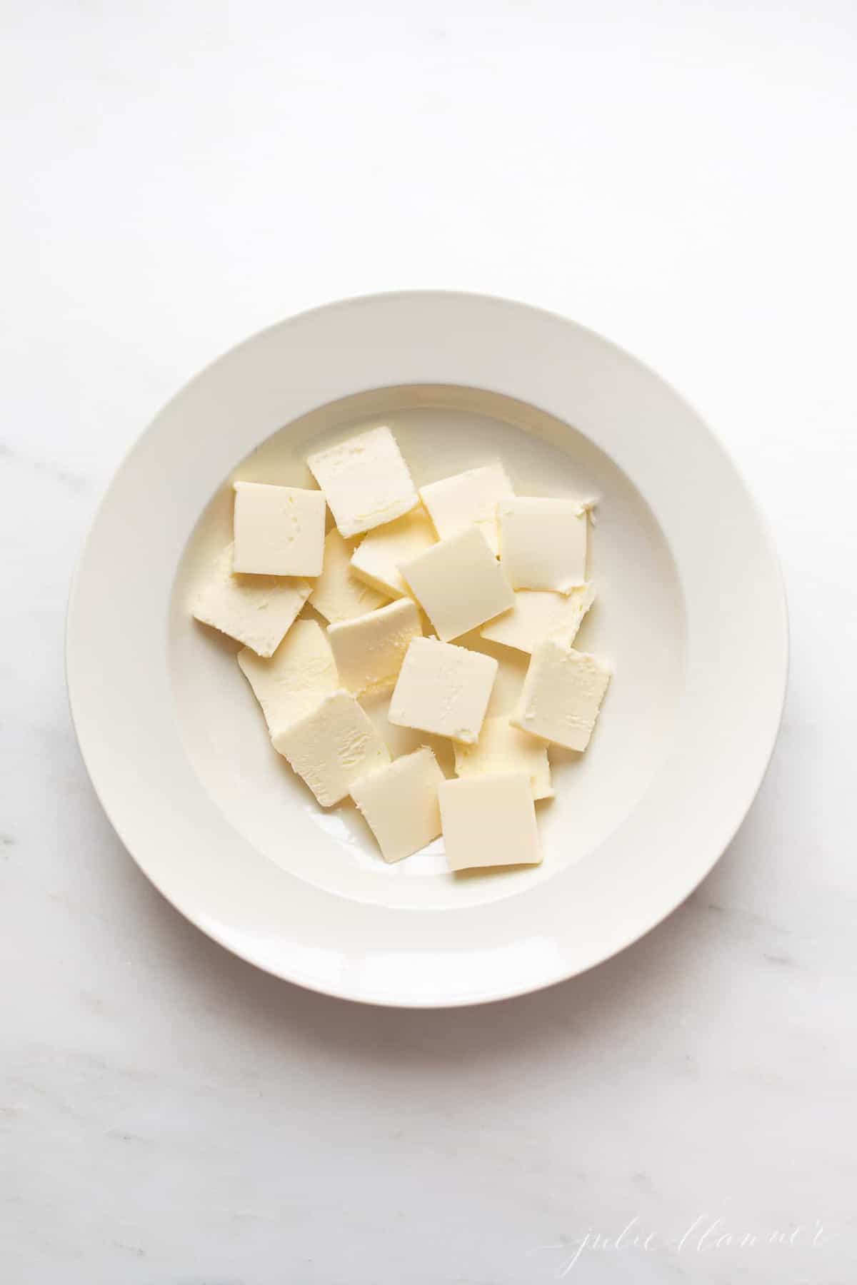A white surface, with a white plate full of cuts of cold butter.