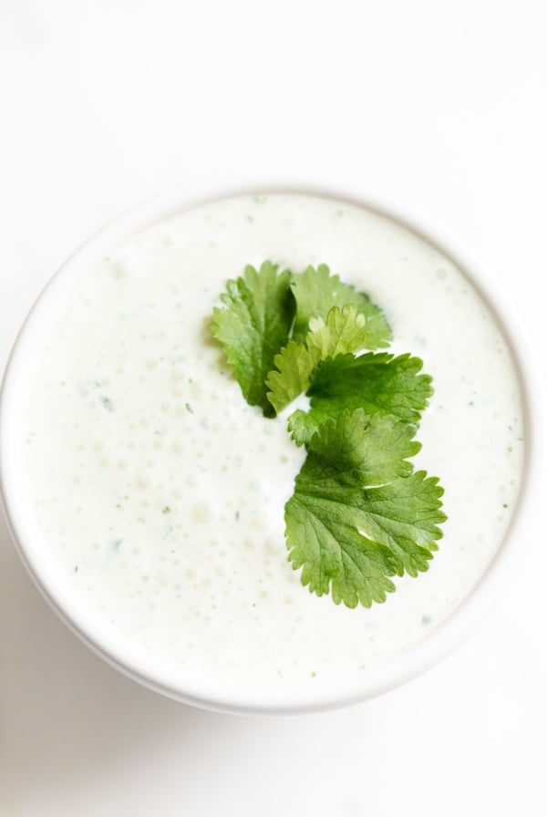 A white bowl of crema de cilantro on a white countertop, garnished with cilantro.