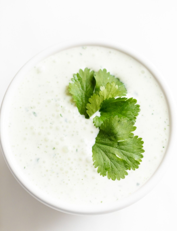 A white bowl of crema de cilantro on a white countertop, garnished with cilantro.