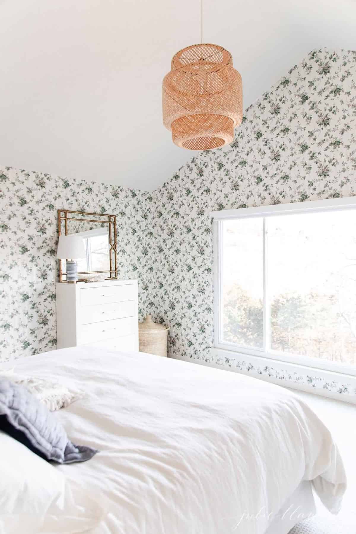 A white bedroom with wooden accents and a statement floral wallpaper. 