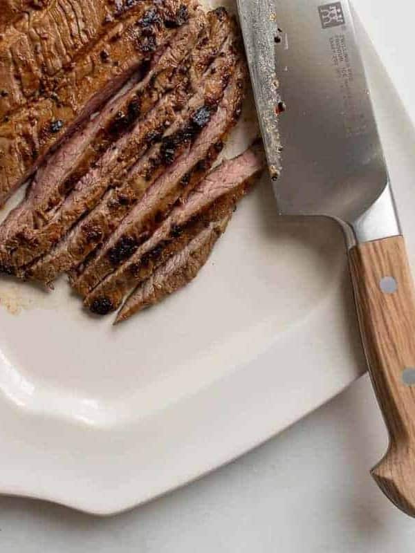 Steak being thinly sliced on a white platter.