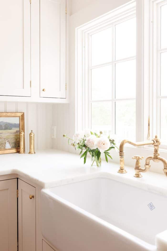 A kitchen sink with a brass faucet and a white peony flower arrangement to the side.