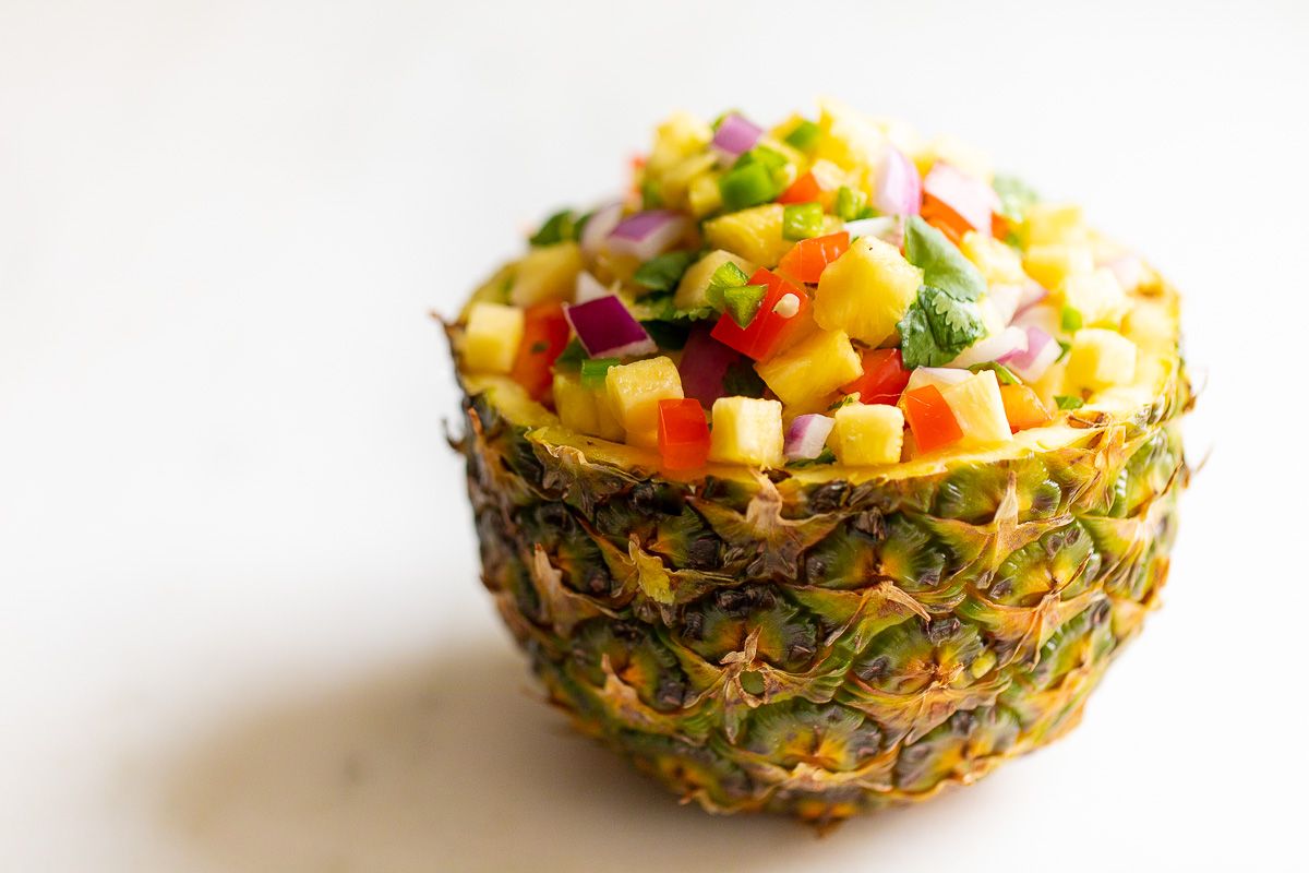 Pineapple salsa inside a pineapple bowl, on a white countertop.